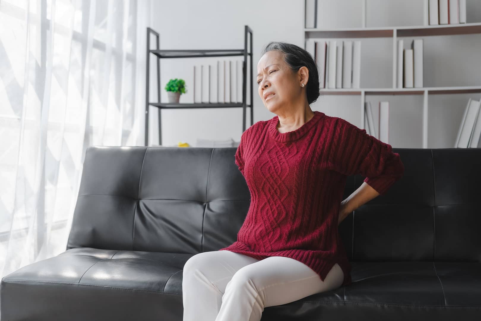 Elderly asian housewife woman sitting on sofa. Back pain, lumbar pain, cervical spine